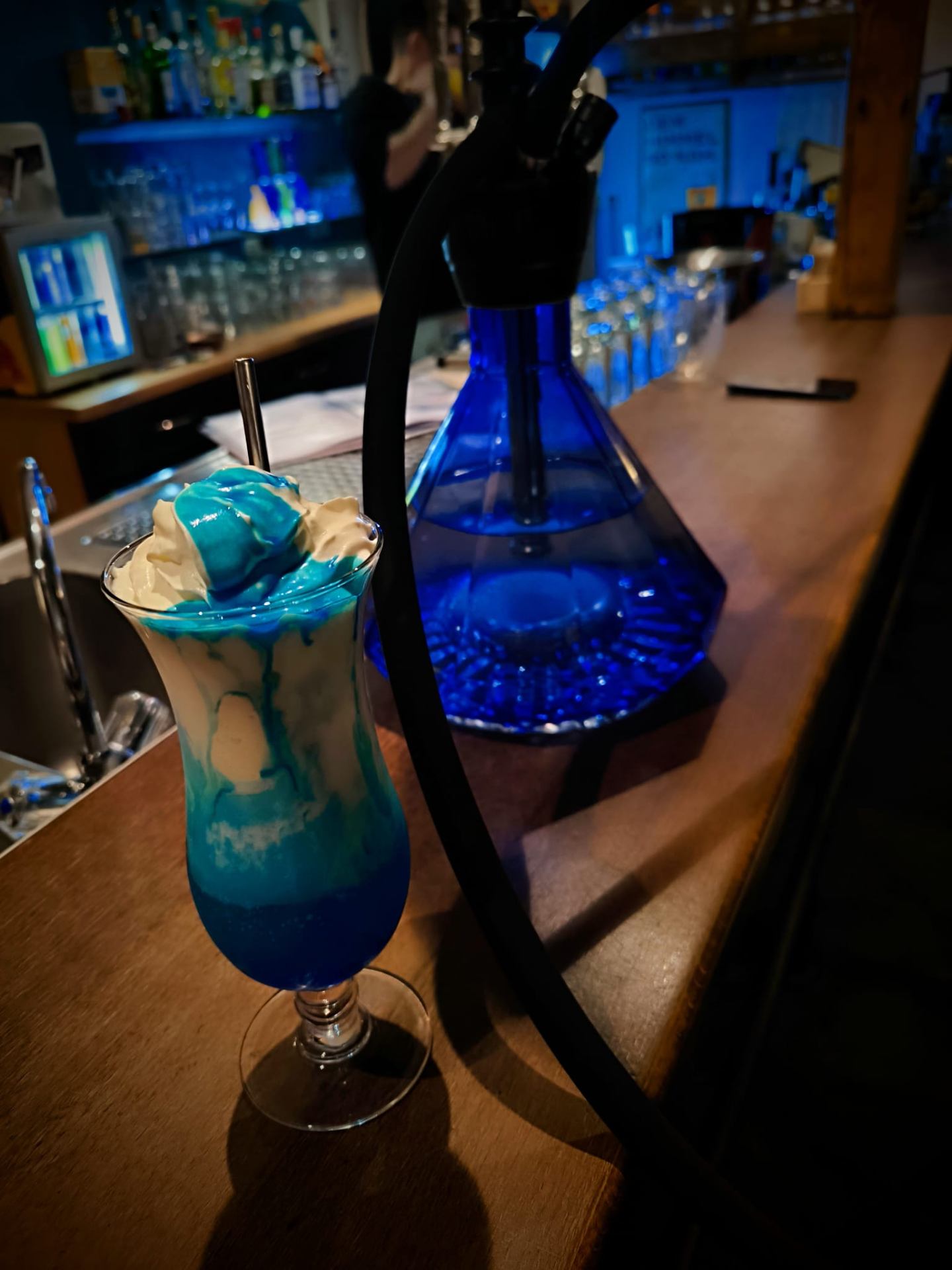 Blauer Signature-Cocktail an der beleuchteten Bar